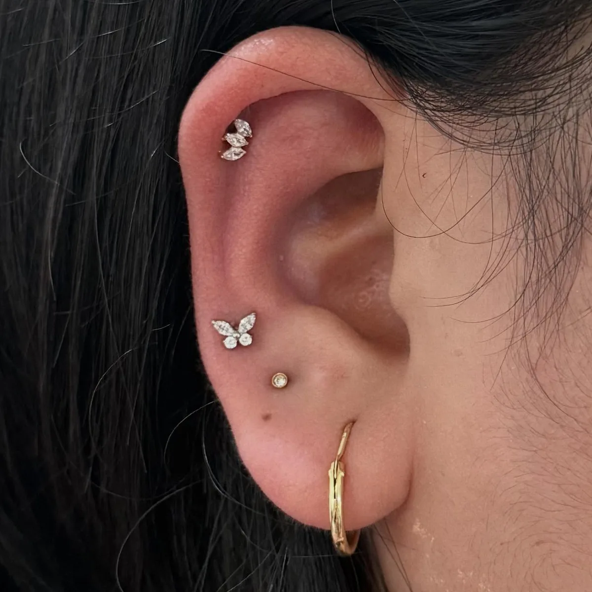 Ear stack with a marquise crystal helix stud, butterfly stud, tiny bezel gem, and a gold hoop on the lobe