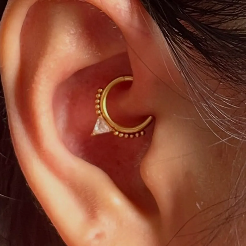 Daith piercing with a gold beaded ring holding a triangular crystal