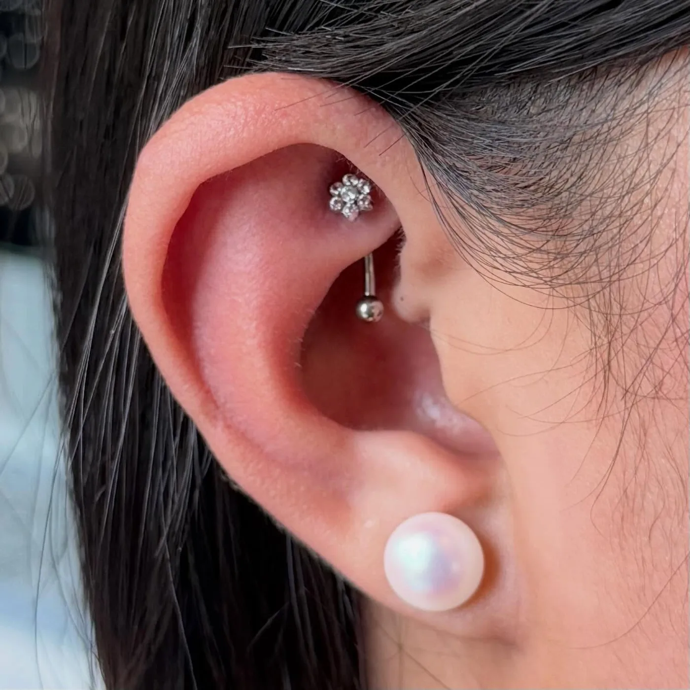 Rook piercing with a silver crystal-flower curved barbell and a pearl stud on the lobe