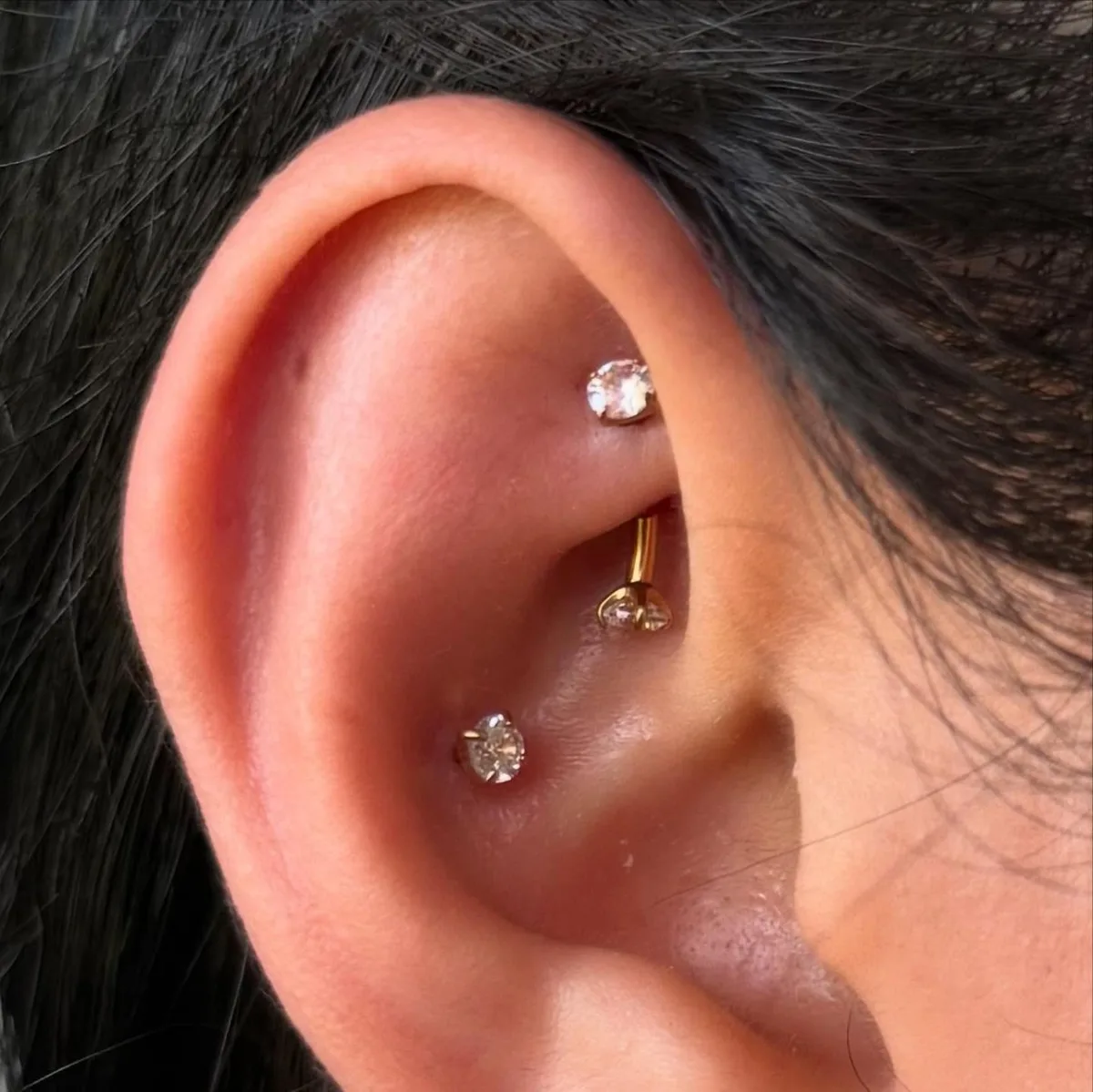 Rook piercing with a gold curved barbell tipped with crystals, plus a crystal conch stud
