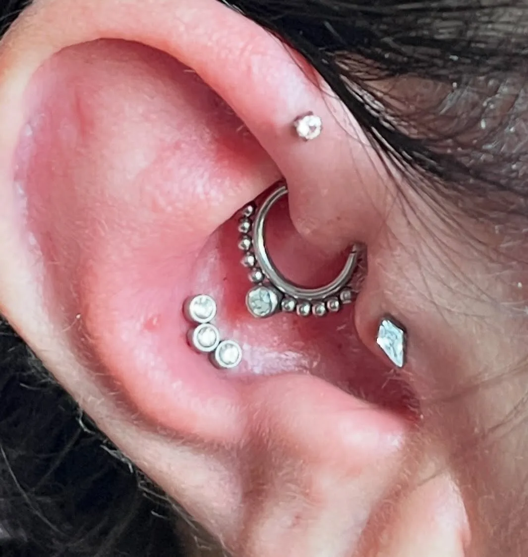 Curated ear with a silver beaded daith ring, curved crystal cluster, and tragus and helix studs