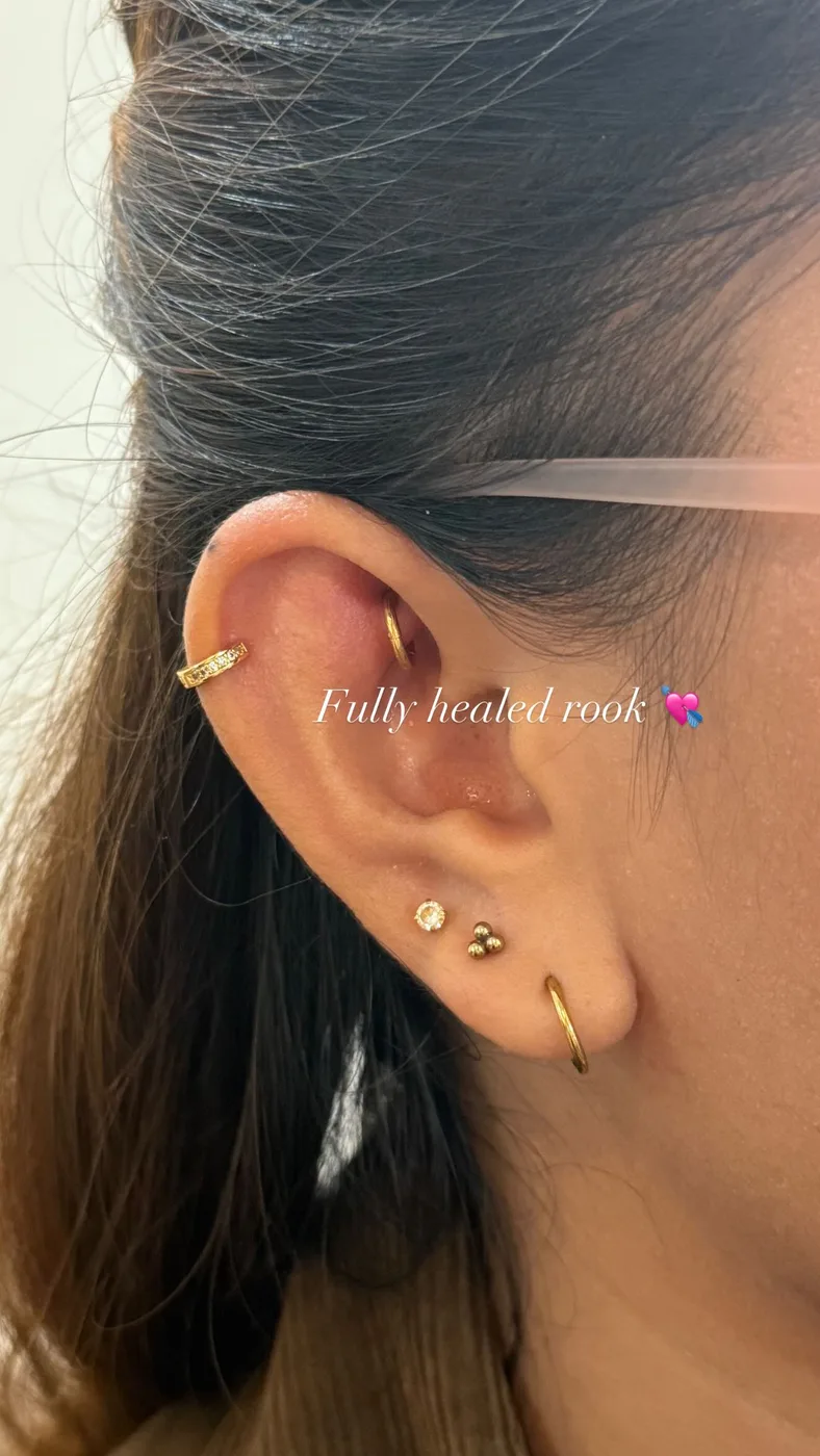 Fully healed rook piercing with a gold hoop, beside a pave helix huggie and stacked lobe studs