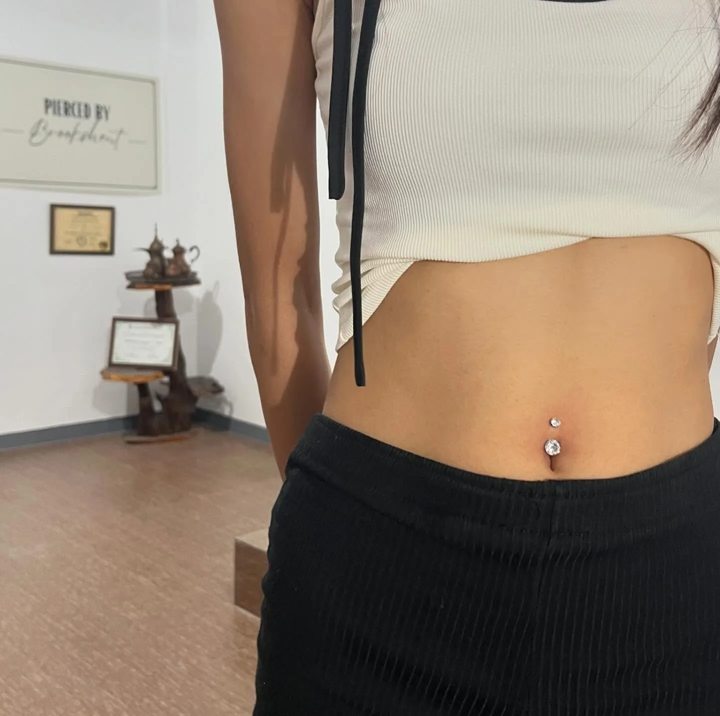 Navel piercing with a silver double crystal barbell, shown in the Pierced by Brookshent studio